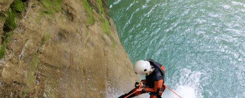 Randonneur en cordage sur falaise près d'une eau turquoise.