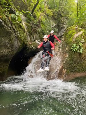 Deux personnes en VTT canyoning sautant dans une gorge couverte de mousse.