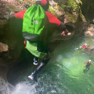 Saut en canyoning dans une eau claire entourée de rochers greenery.