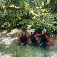 Groupe de trois sportifs en canyoning dans une eau claire entourée de forêt.
