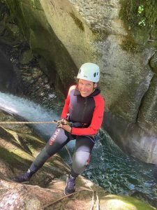 Personne en descente canyoning avec casque et combinaison rouge et noire.